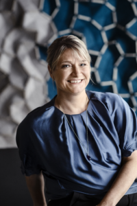 White woman in half figure, smiling at the camera. Artistic blue background.